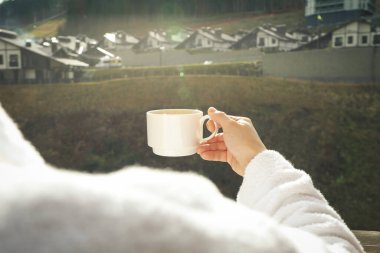 Kayak merkezinin balkonunda elinde kahve olan bir kadın.