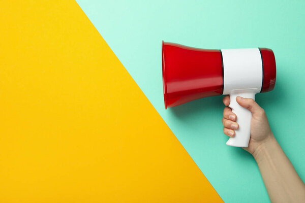 Female hand holds megaphone on two tone background