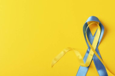Support Ukraine concept, blue and yellow awareness ribbons on yellow background