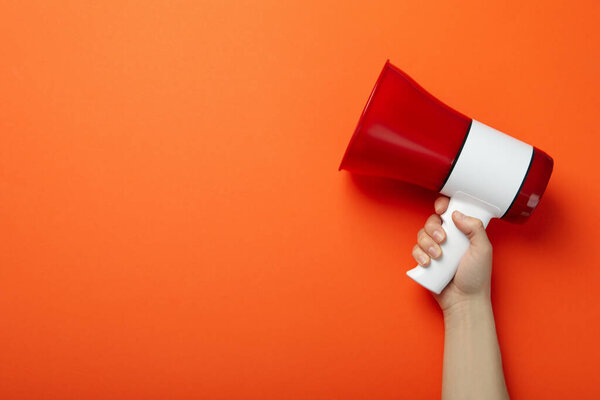 Female hand holds megaphone on orange background