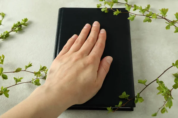 Female hand on Bible and twigs on light textured background