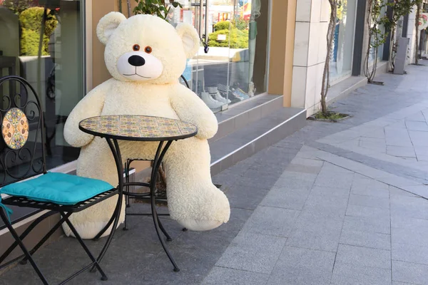 Big teddy bear sitting on chair near cafe