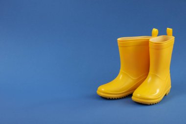 Rubber boots on blue background, space for text