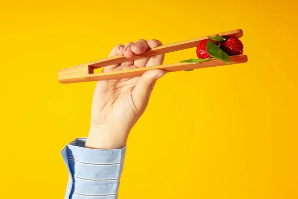 Female Hand Holds Salad Strawberry Wooden Tongs Yellow Background —  Fotos de Stock