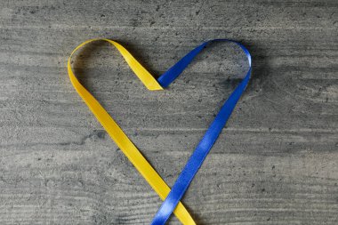 Heart made of ribbons in Ukrainian flag colors on gray wooden background