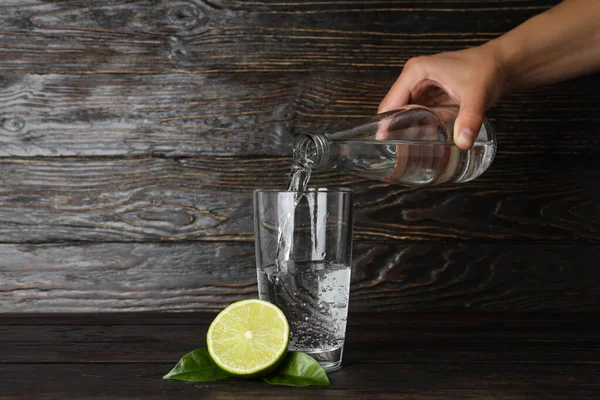 Female hand pour water in glass on wooden background
