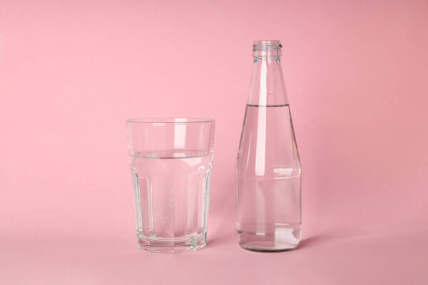 Bottle and glass of water on pink background