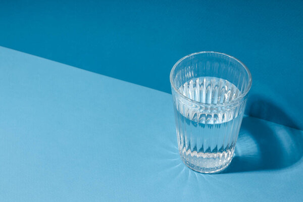 Glass of water on blue background, space for text