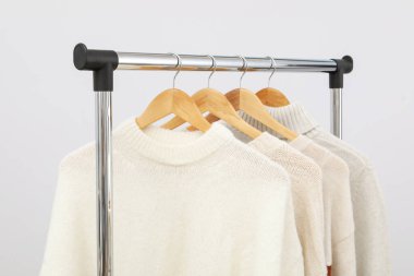 Wardrobe rack with hangers with sweaters on light background