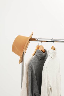 Wardrobe rack with hangers with clothes and hat on light background