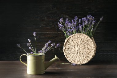 Watering can and wicker bag with lavender flowers on wooden table