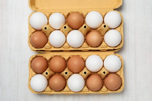 Egg boxes with eggs on white wooden background