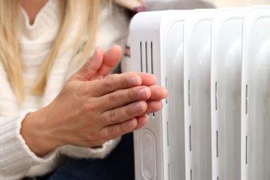 Heating season, woman warms her hands with heater