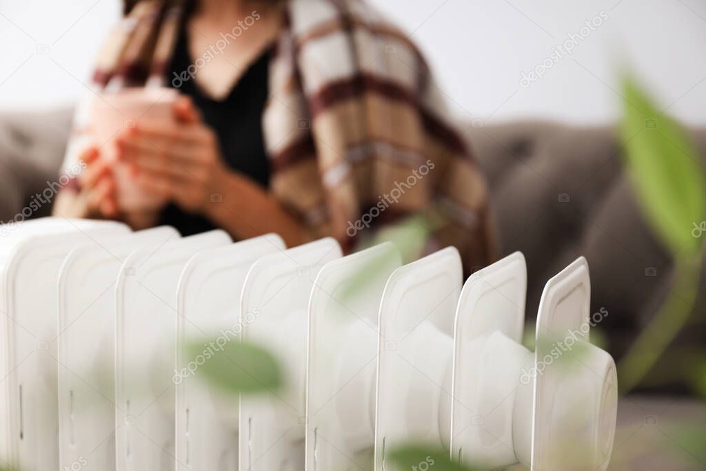 Heating season, heater and woman with plaid on background, selective focus