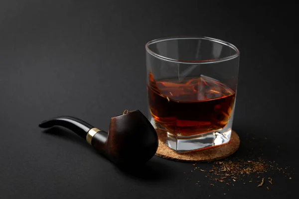Smoking pipe, tobacco and glass of alcohol on black background