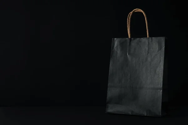 Black paper bag on black background, space for text