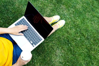 Dizüstü bilgisayarda çalışan ve dışarıdaki çimlerde oturan bir kız.