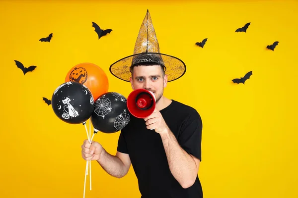 Concept of Halloween, Guy with Halloween balloons and megaphone on yellow background