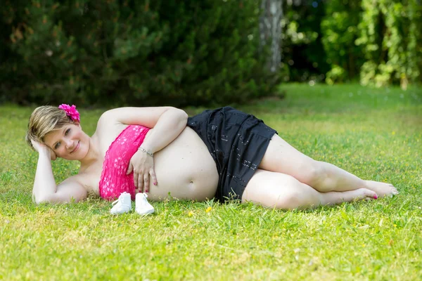 Terhes nő, fekvő, zöld fűben — Stock Fotó