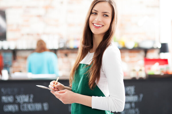 Young waitress holding notepad in cafe