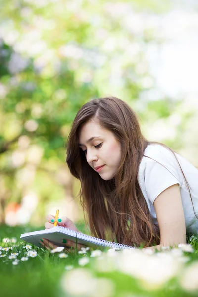 Girl lying on grass with workbook — Stock Photo, Image