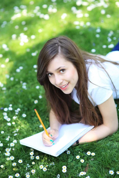 Chica acostada en la hierba con libro de trabajo — Foto de Stock