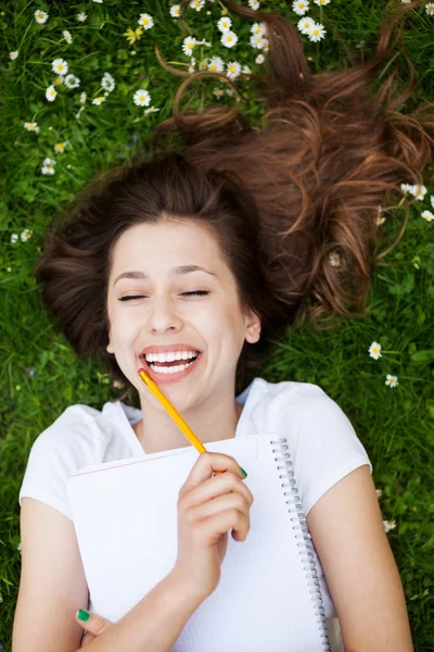 Chica acostada en la hierba con libro de trabajo — Foto de Stock