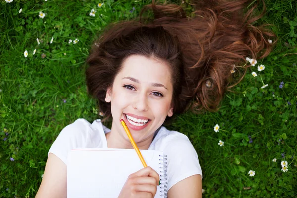 Flicka ligger på gräset med arbetsbok — Stockfoto