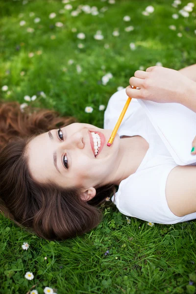 Flicka ligger på gräset med arbetsbok — Stockfoto
