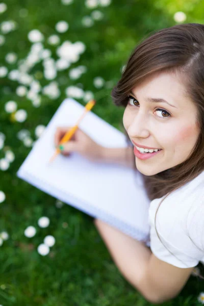 Chica acostada en la hierba con libro de trabajo — Foto de Stock