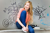 Young woman sitting in front of graffiti