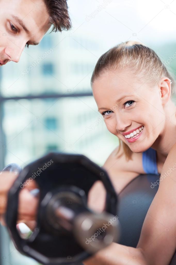 Woman lifting dumbbells while instructor assisting her