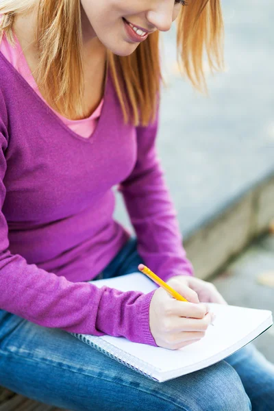 Kvinnlig student skriver i anteckningsboken — Stockfoto
