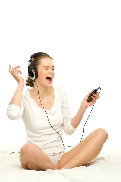 Kvinna sitter på sängen, lyssna på musik i hörlurar — Stockfoto
