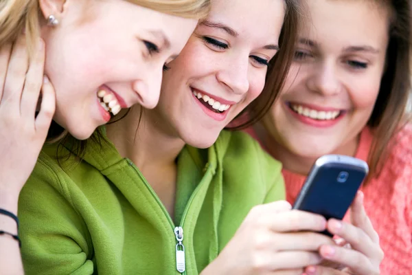 Tre kvinnliga vänner skrattar och tittar på mobilen — Stockfoto