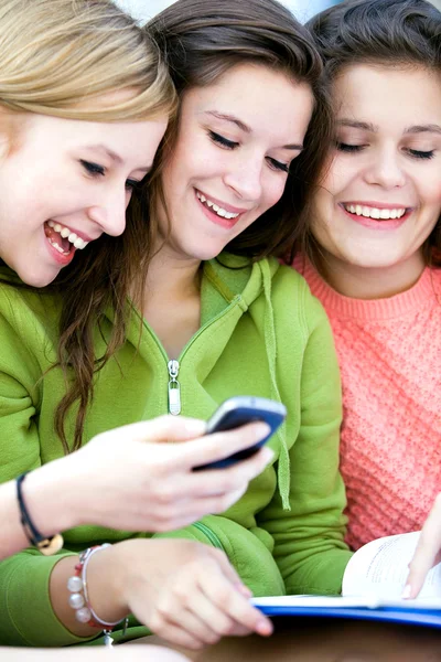 Drie vriendinnen lachen en kijken naar mobiele telefoon — Stockfoto