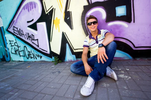 Young man sitting against graffiti wall — Stock Photo, Image