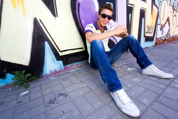 Young man sitting against graffiti wall — Stock Photo, Image