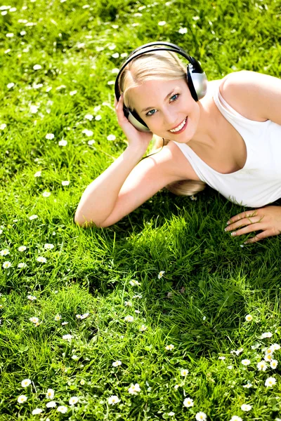 Ung kvinna på gräs som lyssnar på musik — Stockfoto