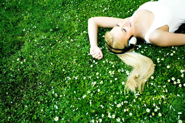Kvinna liggande på gräs med hörlurar — Stockfoto