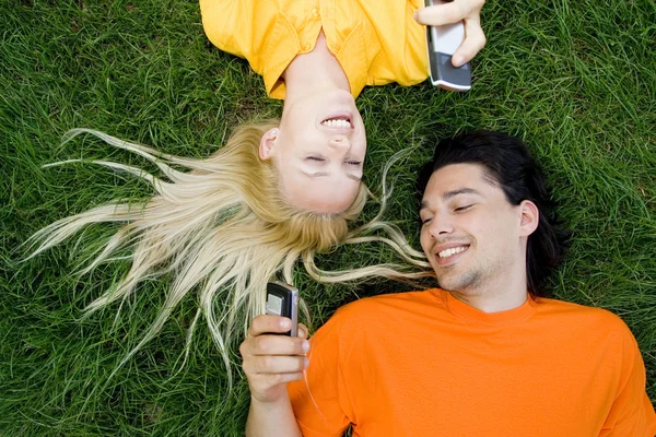 Par liggande i gräset med mobiltelefoner — Stockfoto