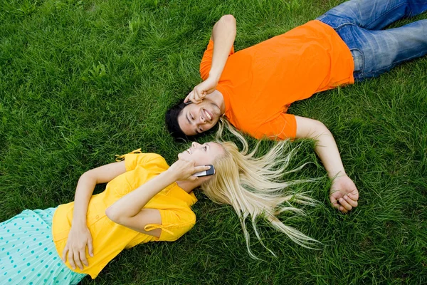 Pareja acostada en la hierba con teléfonos móviles — Foto de Stock