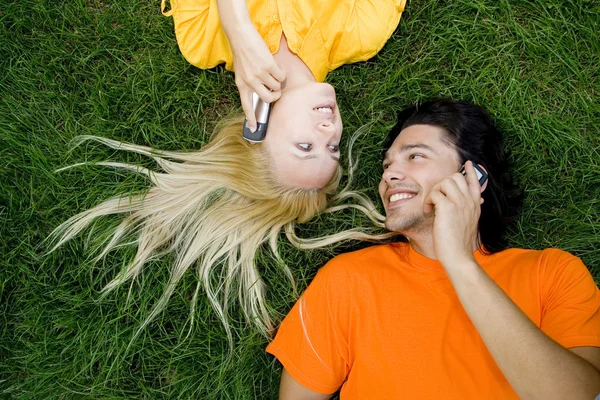 Par liggande i gräset med mobiltelefoner — Stockfoto