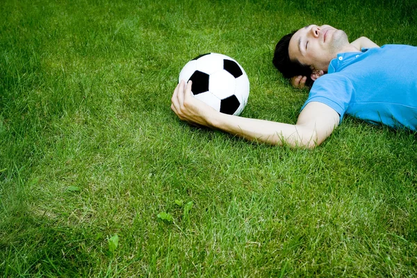 Jeune homme allongé sur l'herbe avec ballon de football — Photo