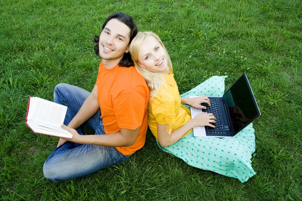 Students sitting back to back on grass Royalty Free Stock Images