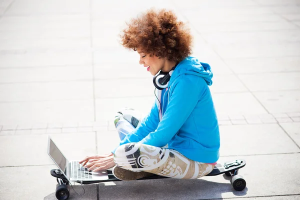 Женщина сидит на скейтборде с ноутбуком — стоковое фото