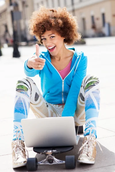 Woman sitting on skateboard with laptop — Stock Photo, Image
