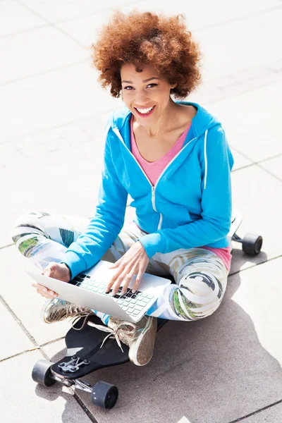 Woman sitting on skateboard with laptop — Stock Photo, Image