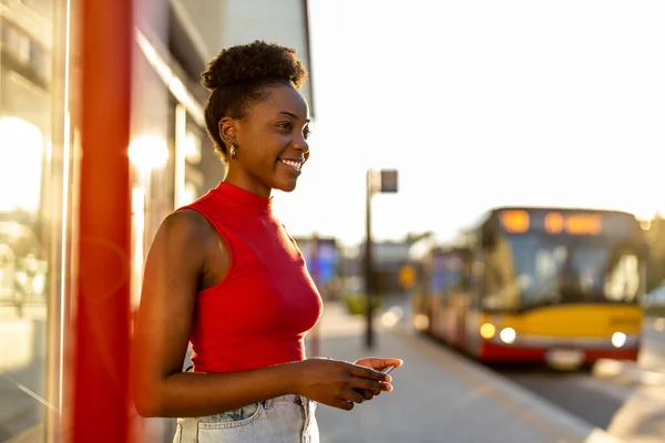 Young woman with smartphone waiting at the bus stop