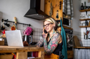 Tekerlekli sandalyedeki dövmeli kadın evde dizüstü bilgisayarla çalışıyor.